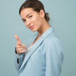 A young woman in a blue suit exhibits confidence with a relaxed pose against a blue background.